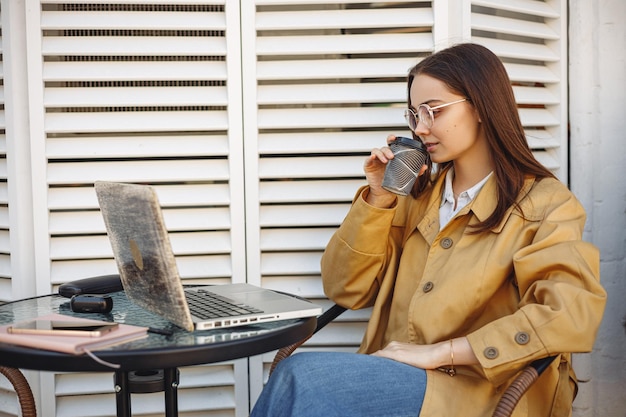 Female freelancer drinking coffee and looking at screen of\
laptop while having break in work