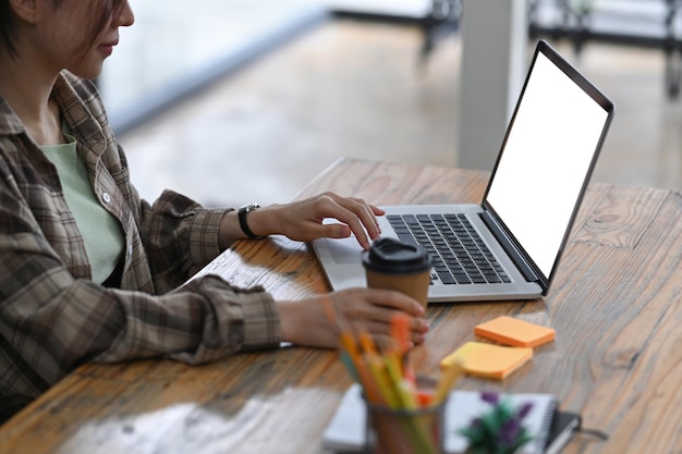 Female freelancer holding coffee cup and working with computer laptop on wooden table