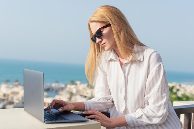 A female freelancer is working on a laptop with a sea view