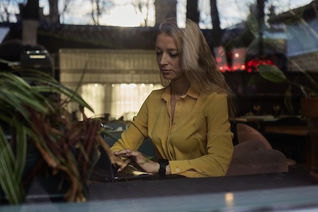 카페 밖에 있는 유리창 너머로 탁자에 앉아 있는 여성 프리랜서