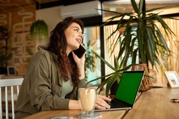 Женщина-фрилансер разговаривает по телефону, делая покупки в Интернете, молодая девушка, работающая в кафе