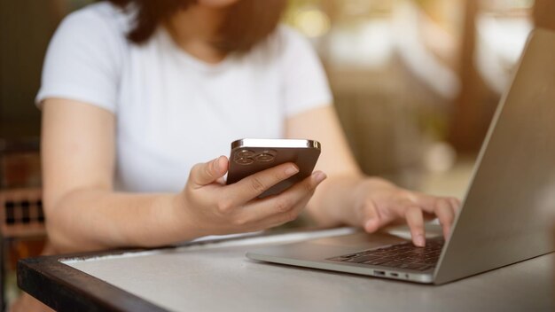 A female freelancer using her smartphone and laptop working remotely at a coffee shop