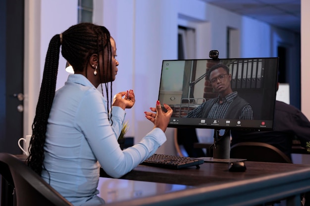 女性フリーランサーは、コンピューターでオンライン ビデオ通話会議を使用して、スタートアップ ビジネスについてマネージャーと話します。リモート ビデオ会議で会議を行い、勤務時間外にオフィスで夜間に作業します。