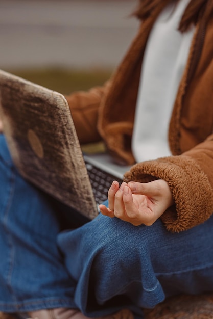 Female freelancer with yoga mudra sitting with laptop and\
meditating during break in work in nature