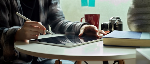 female freelancer working on digital tablet with stylus pen on coffee table beside window
