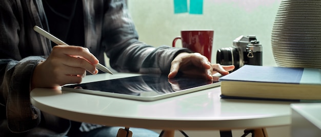 Female freelancer working on digital tablet with stylus pen on coffee table beside window