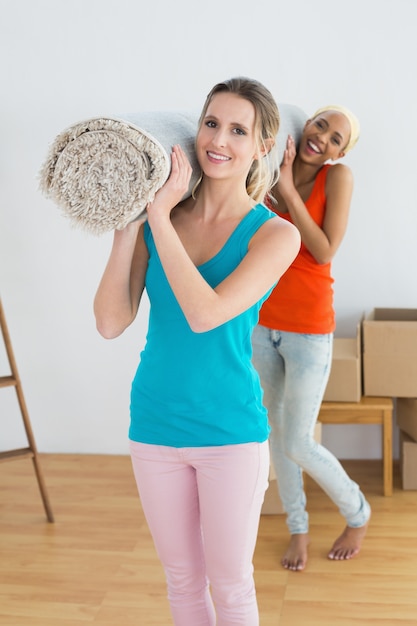 Female friends carrying rolled rug after moving in a house