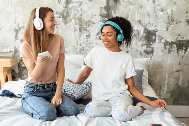 Female friends dancing together on bed at home