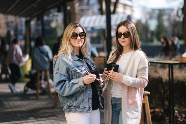 Female friends eat asian food takeaway in the street