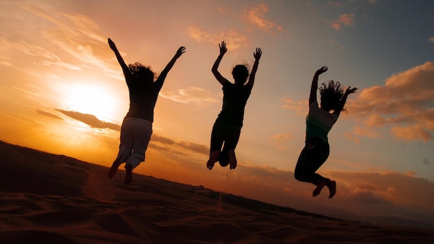 female friends jumping at beach against sky during sunset
