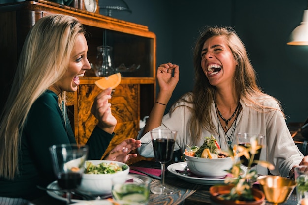 Female friends laughing while having food and drinks at table