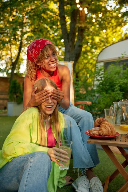 Female friends at outdoor picnic celebrating summertime vacation drinking lemonade eating sweets