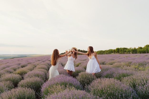 female friends standing on the lavender field and clinking glasses of wine