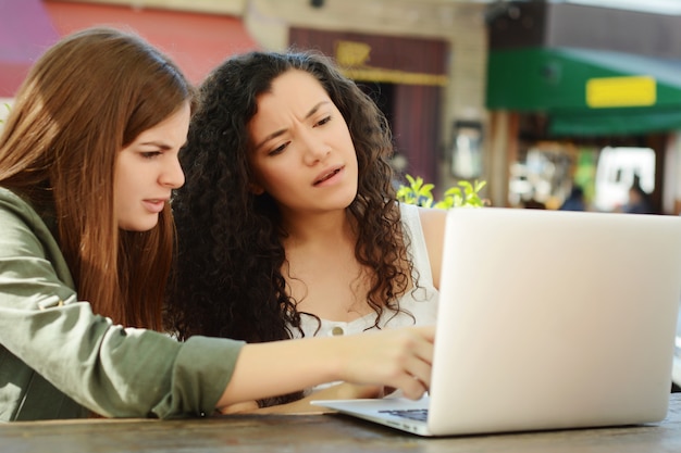 Amici femminili che studiano con un computer portatile in una caffetteria.