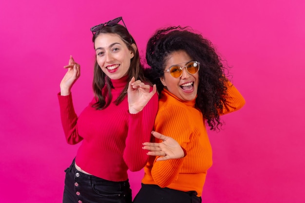 Female friends in sunglasses having fun and dancing on a pink background studio shot lifestyle