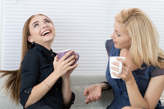 Female friends talking and drinking coffee while sitting on sofa