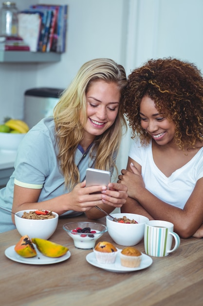 Female friends using cellphone during breakfast 