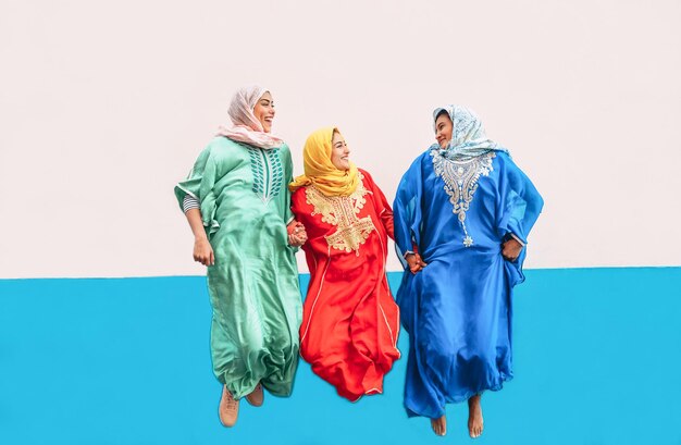 Foto amici donne che indossano abiti tradizionali che saltano contro il muro