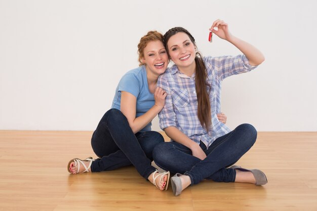 Female friends with house keys sitting on the floor