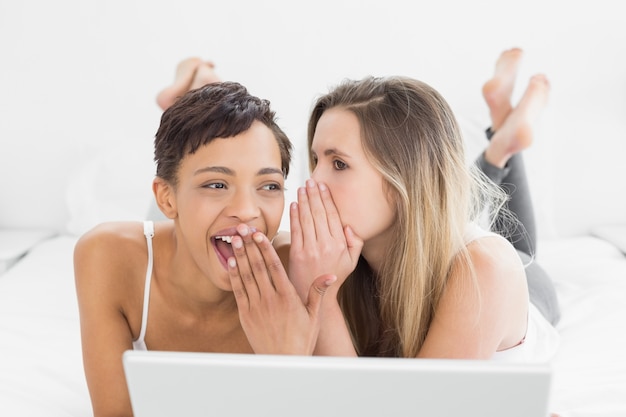 Female friends with laptop gossiping in bed