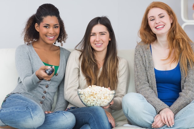 Amici femminili con telecomando e ciotola di popcorn sul divano