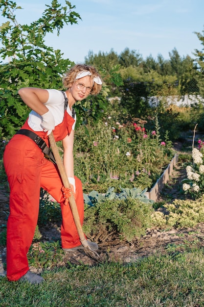 female gardener in gloves and an apron stands against the background of flower bed in a home garden