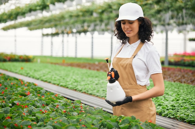 Female gardener standing at greenhouse with water sprayer