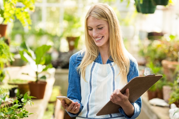 Female gardener using cellphone while holding clipboard