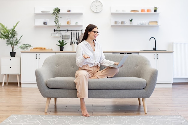 Female gesturing with hands while sitting on couch with modern laptop