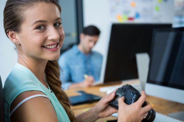 Female graphic designer holding digital camera at desk