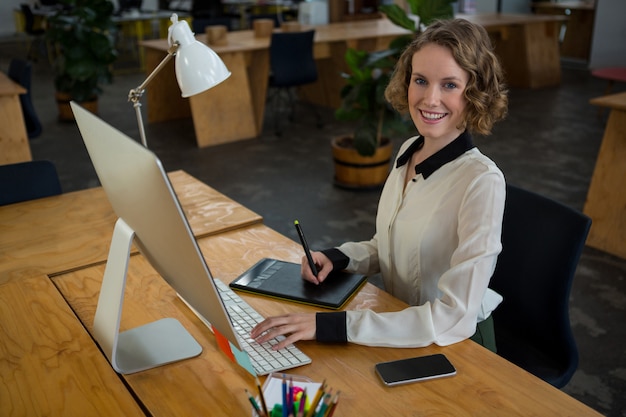 Female graphic designer smiling while using desktop pc and graphic tablet