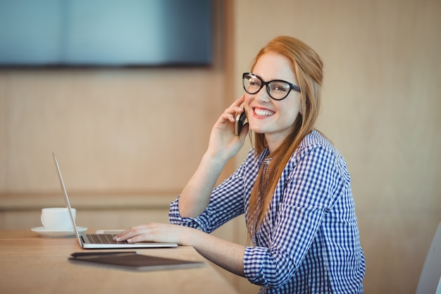 オフィスで働いている間携帯電話で話している女性のグラフィックデザイナー