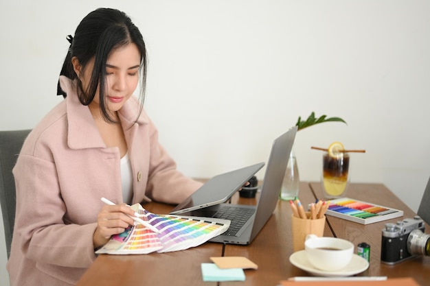 Женщина-графический дизайнер, работающая над своим проектом, проверяет образцы цветов на своем столе