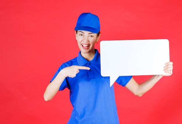 Female guide in blue uniform holding a white rectangular info board. 