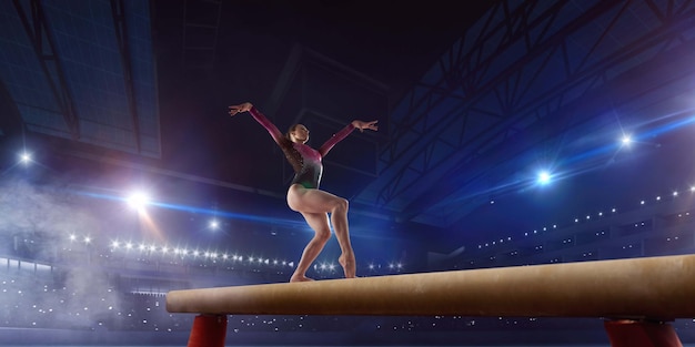 Female gymnast doing a complicated trick on gymnastics balance beam in a professional arena