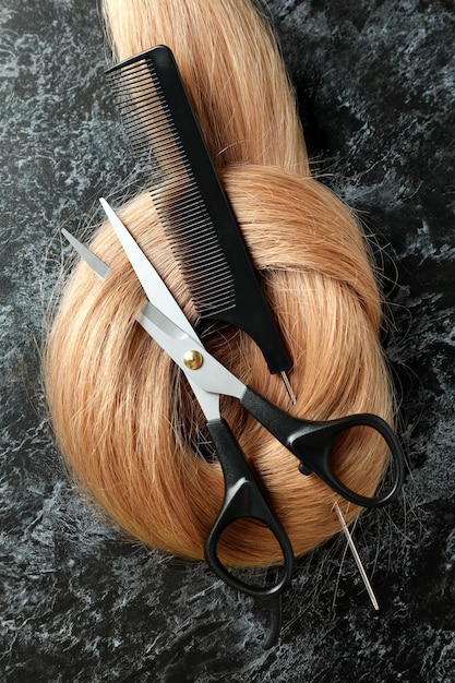 Female hair with scissors and hairbrush on dark background