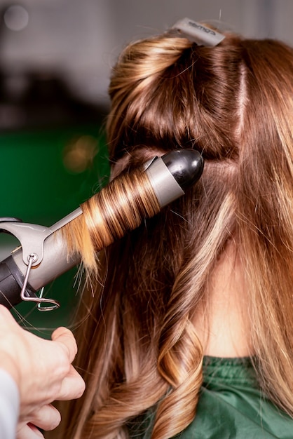 La parrucchiera sta arricciando i capelli per una giovane donna caucasica dai capelli castani in un salone di bellezza