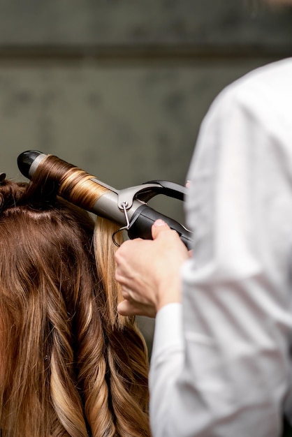 The female hairdresser is curling hair for a brownhaired young caucasian woman in a beauty salon