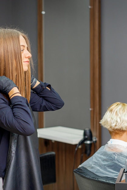 Женский парикмахер надевает черный фартук перед стрижкой клиентки