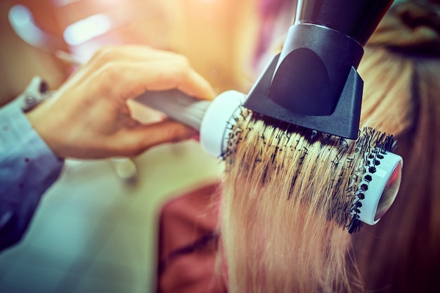 Female hairdresser using hairbrush and hair dryer