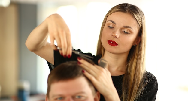 Female Hairstylist Cutting Hair of Man Client. Woman Hairdresser Holding Scissors in Hand. Young Stylist Making Haircut for Male Customer. Guy Getting Hairdo in Beauty Salon. Beautician Styling Hair