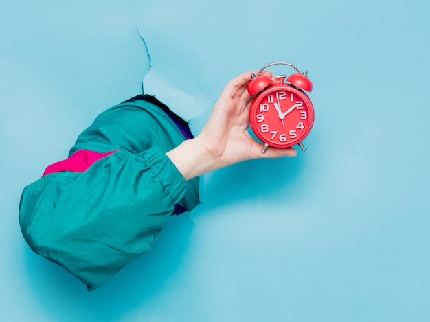 female hand in 90s style jacket holding alarm clock 