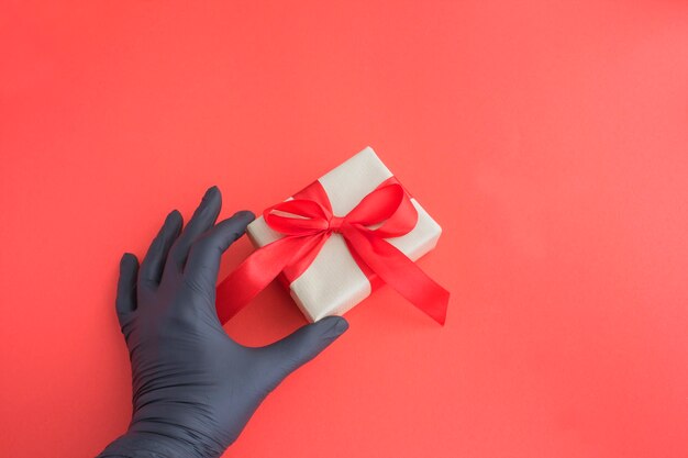 Mano femminile in un guanto nero con confezione regalo sul rosso