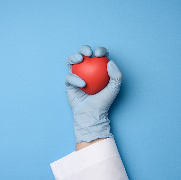 Photo female hand in blue latex gloves holding a red heart, donation concept, top view