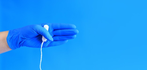 Female hand in a blue latex medical glove holds a tampon feminine personal hygiene product