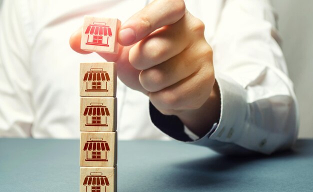 Photo female hand builds a tower of blocks with store icons building a business empire