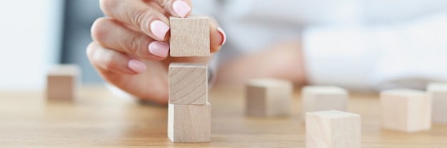 Female hand builds tower from wooden cubes