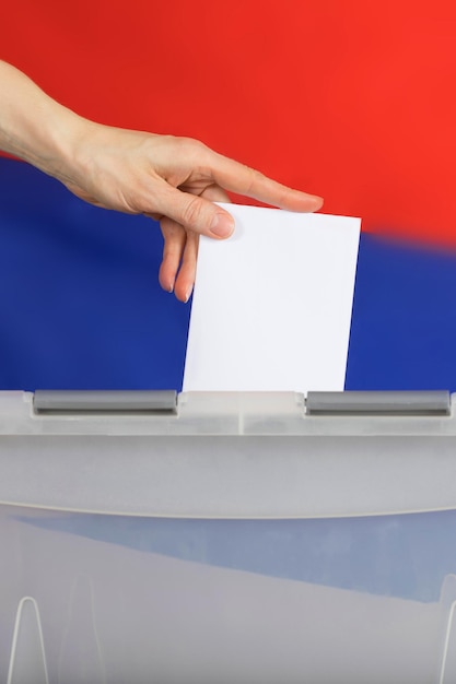 Фото Женская рука бросает бюллетень в урну для голосования. на заднем плане российский флаг.