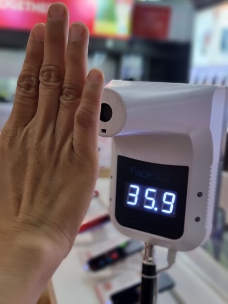 Foto mano femminile che controlla la temperatura corporea con il termometro digitale a infrarossi con le mani