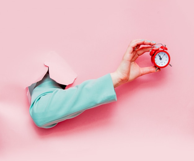 Female hand in classic blue jacket with red alarm clock 